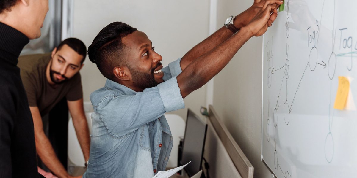 A team of professionals actively collaborating around a whiteboard, discussing solutions to a complex problem, reflecting project-based learning.